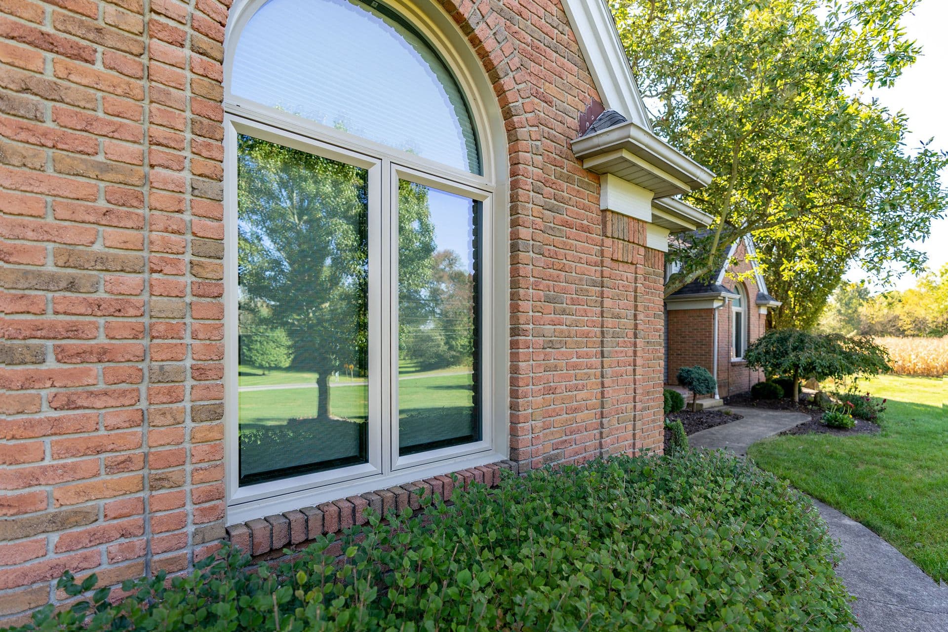 Large arched window and adjacent sliding glass doors on brick home exterior, reflecting surrounding landscaped yard with mature trees