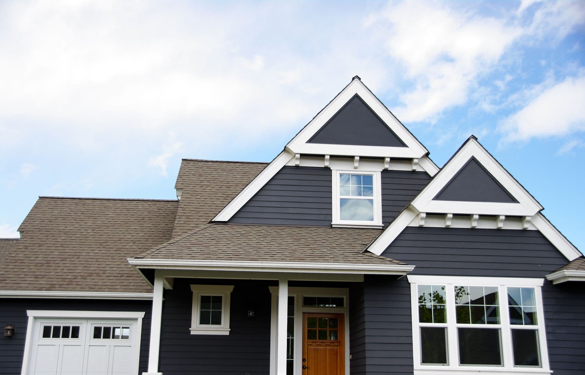 Two-story home with dark blue siding, white trim, and dual gabled roofline featuring dormer window and attached garage
